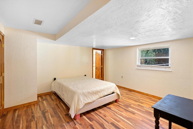 bedroom with wood finished floors, visible vents, baseboards, a textured ceiling, and a textured wall