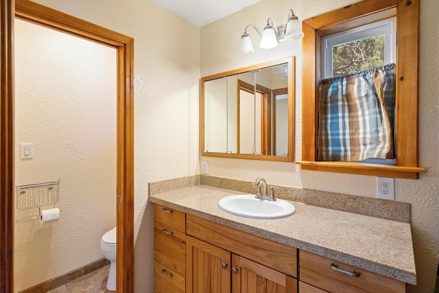 bathroom with vanity, toilet, and a textured wall