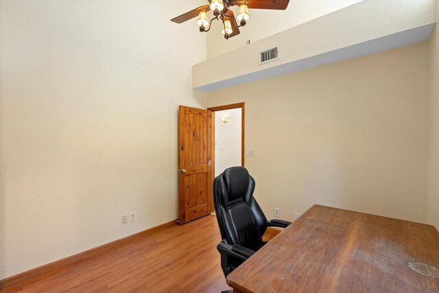 office with visible vents, a towering ceiling, light wood-style floors, baseboards, and ceiling fan