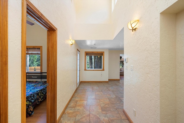 hallway featuring stone finish floor, a textured wall, and baseboards