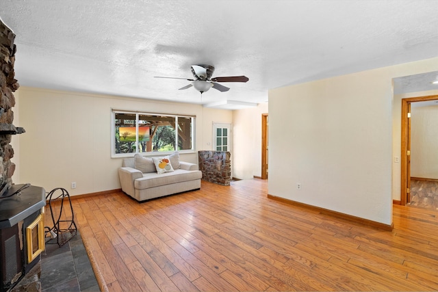 living room featuring a ceiling fan, hardwood / wood-style flooring, a textured ceiling, baseboards, and a wood stove