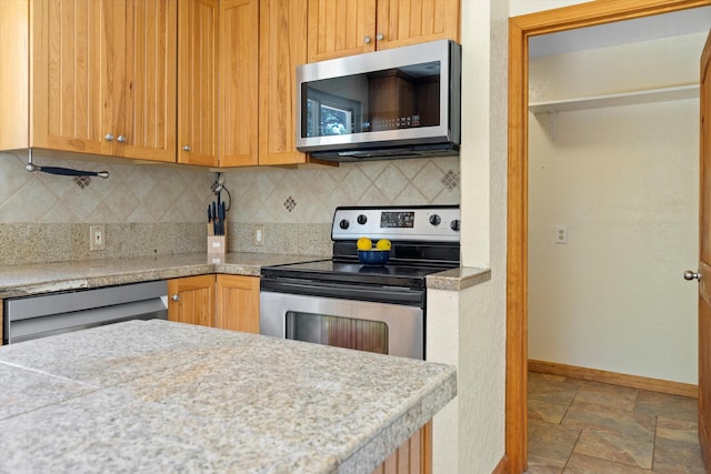 kitchen with stone finish floor, tasteful backsplash, stainless steel appliances, light countertops, and baseboards