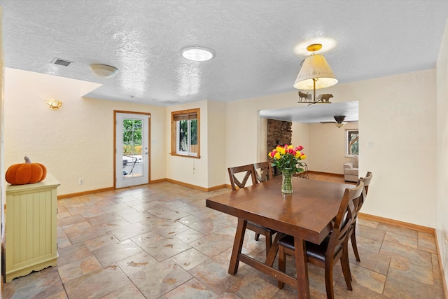 dining area with visible vents, baseboards, a textured ceiling, and stone tile flooring