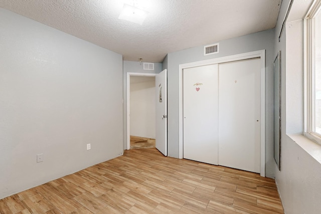 unfurnished bedroom with light wood-style flooring, visible vents, a closet, and a textured ceiling