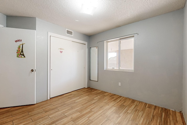 unfurnished bedroom featuring visible vents, a textured ceiling, a closet, and light wood finished floors