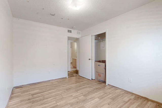 unfurnished bedroom with a closet, visible vents, a textured ceiling, and light wood-type flooring