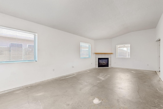 unfurnished living room featuring a tile fireplace, unfinished concrete floors, and vaulted ceiling