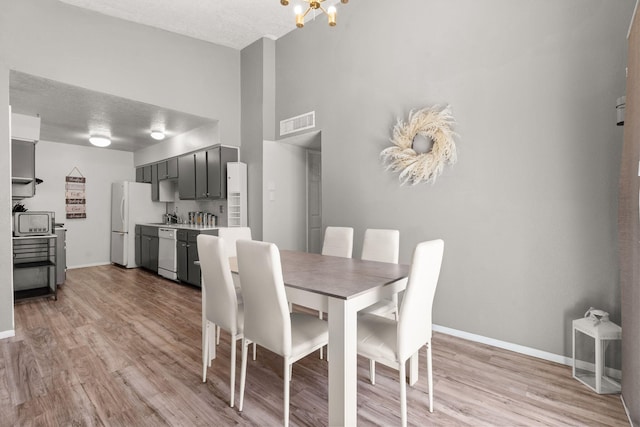 dining room featuring light wood-type flooring, visible vents, baseboards, and a textured ceiling