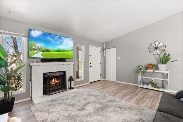 living area featuring a brick fireplace, wood finished floors, baseboards, and vaulted ceiling