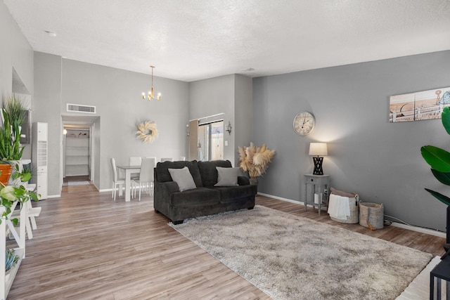 living room featuring visible vents, a notable chandelier, a textured ceiling, light wood-style floors, and baseboards