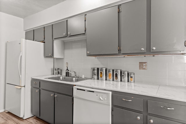 kitchen featuring white appliances, light wood finished floors, gray cabinetry, a sink, and tasteful backsplash