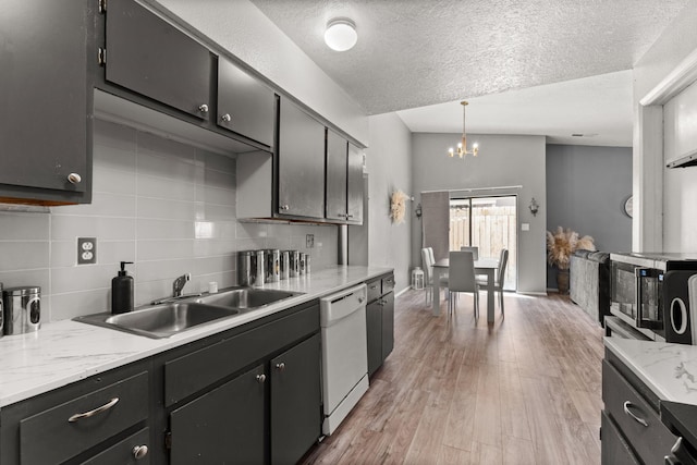 kitchen featuring an inviting chandelier, a sink, light wood-style floors, dishwasher, and backsplash