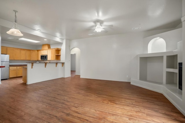 unfurnished living room with visible vents, wood finished floors, arched walkways, and ceiling fan