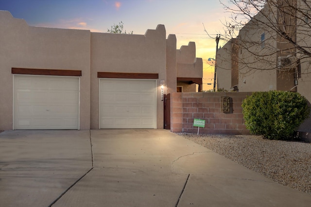 pueblo-style house featuring stucco siding, an attached garage, concrete driveway, and fence