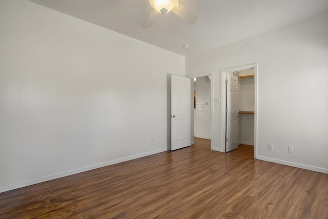 unfurnished bedroom featuring a spacious closet, ceiling fan, baseboards, and wood finished floors