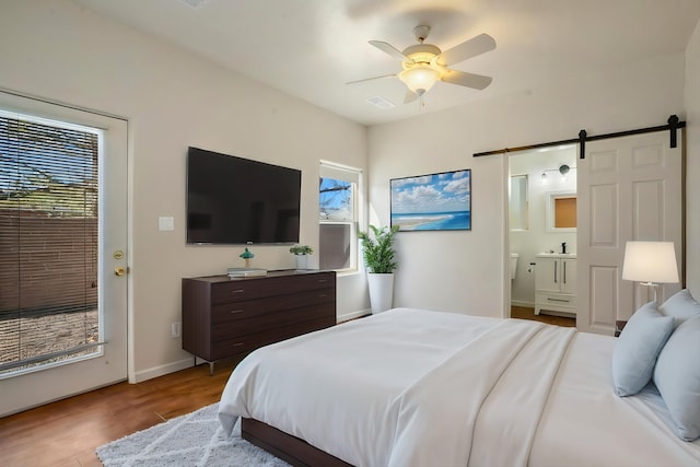 bedroom featuring visible vents, ceiling fan, a barn door, ensuite bathroom, and wood finished floors