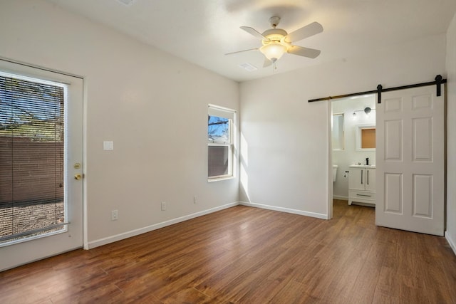 unfurnished bedroom featuring a barn door, wood finished floors, visible vents, and baseboards