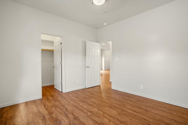 unfurnished bedroom with a walk in closet, baseboards, wood finished floors, a closet, and a ceiling fan