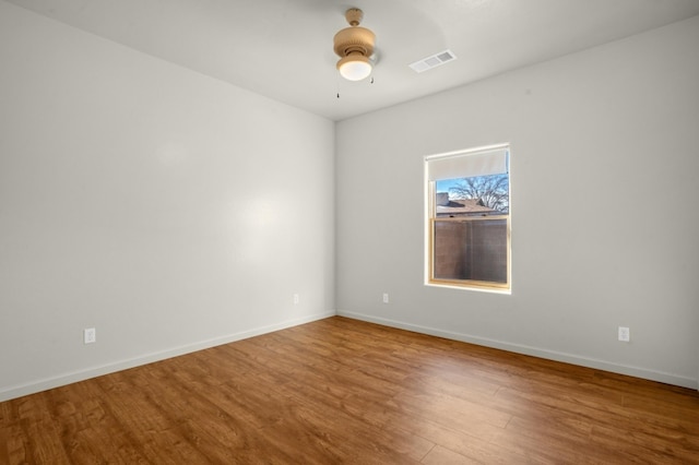 spare room with ceiling fan, visible vents, baseboards, and wood finished floors