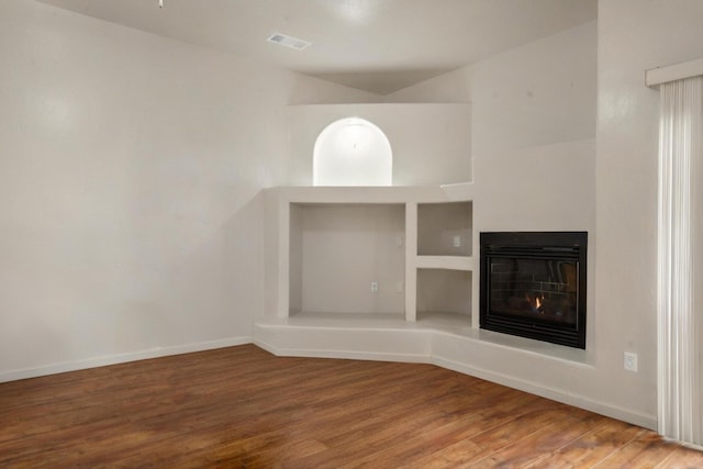 unfurnished living room with visible vents, baseboards, a glass covered fireplace, and wood finished floors