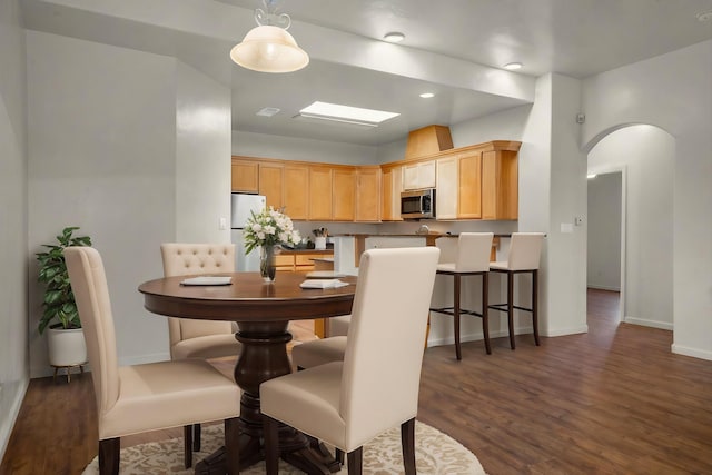 dining area with dark wood-style floors, arched walkways, and baseboards