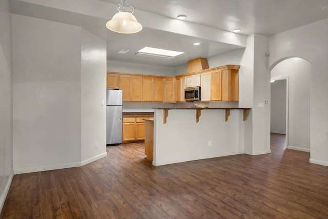 kitchen with a breakfast bar, a peninsula, arched walkways, stainless steel appliances, and dark wood-type flooring