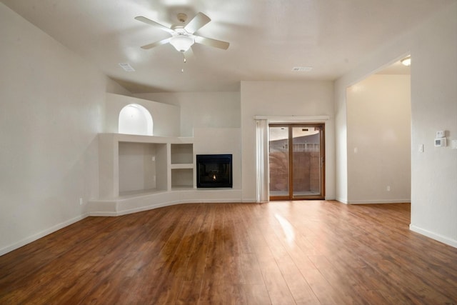 unfurnished living room with a ceiling fan, wood finished floors, baseboards, visible vents, and a glass covered fireplace