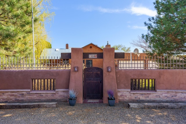 view of front of home with stucco siding, a gate, a fenced front yard, stone siding, and a chimney