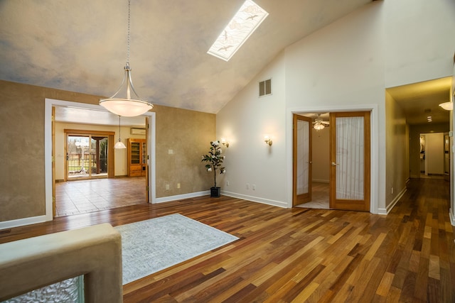 interior space featuring visible vents, high vaulted ceiling, wood-type flooring, a skylight, and baseboards