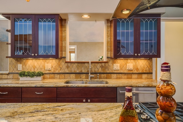 kitchen with decorative backsplash, glass insert cabinets, light stone countertops, and a sink