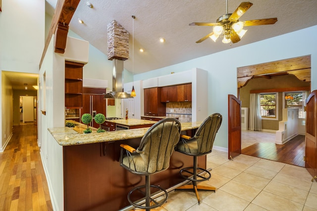 kitchen with ceiling fan, pendant lighting, island range hood, light tile patterned flooring, and a textured ceiling