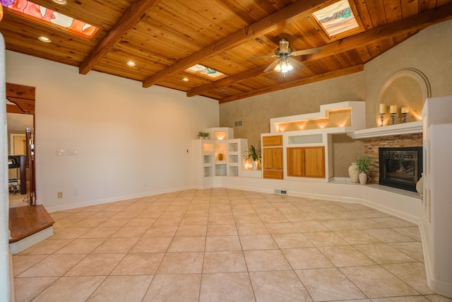 unfurnished living room featuring light tile patterned floors, beam ceiling, a skylight, wood ceiling, and a glass covered fireplace