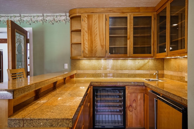 kitchen featuring a peninsula, tile countertops, beverage cooler, and a sink