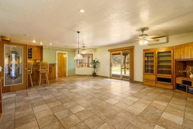 unfurnished living room featuring baseboards, ceiling fan, a textured ceiling, and a wall unit AC