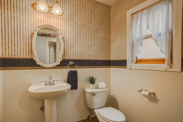 half bath featuring wallpapered walls and toilet