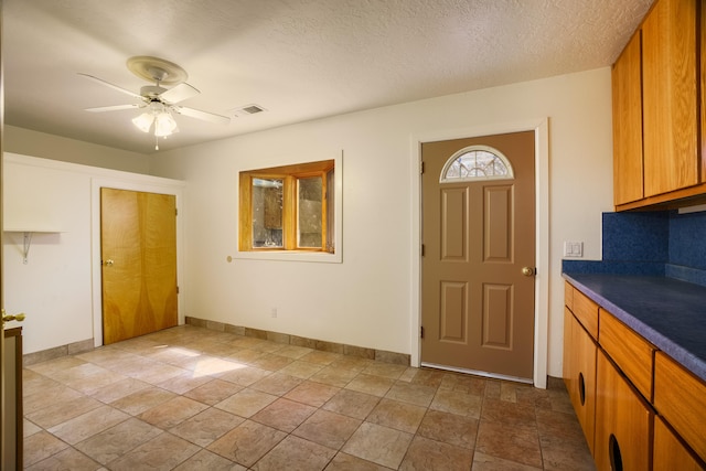 foyer featuring visible vents, baseboards, a textured ceiling, and ceiling fan