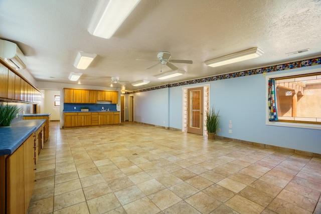 kitchen featuring visible vents, a wall mounted AC, a textured ceiling, dark countertops, and brown cabinets