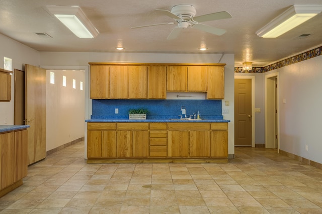 kitchen featuring tasteful backsplash, visible vents, ceiling fan, brown cabinetry, and a sink