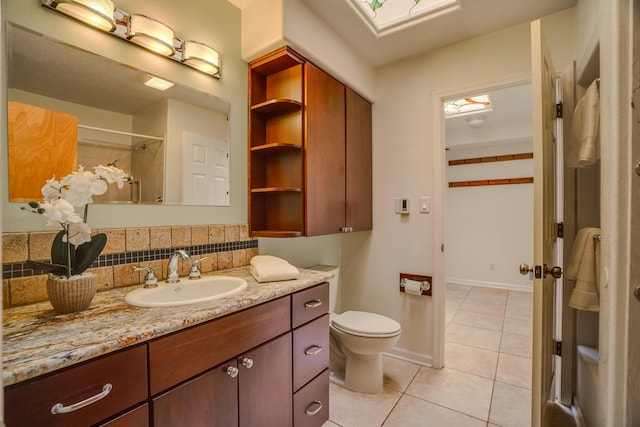 bathroom featuring vanity, a skylight, tile patterned flooring, decorative backsplash, and toilet