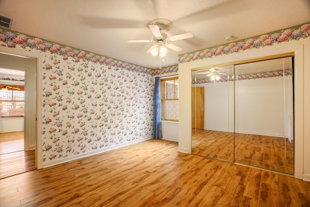 unfurnished bedroom with a ceiling fan, wood finished floors, a closet, wallpapered walls, and baseboards