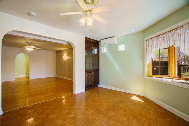 spare room with a ceiling fan, a textured ceiling, a wall unit AC, arched walkways, and baseboards