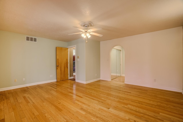 spare room featuring a ceiling fan, baseboards, visible vents, light wood-style flooring, and arched walkways