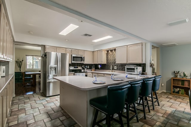 kitchen featuring visible vents, a peninsula, appliances with stainless steel finishes, stone finish flooring, and backsplash