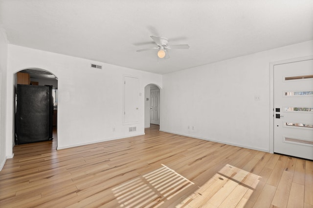 unfurnished living room with visible vents, arched walkways, light wood-style floors, and ceiling fan