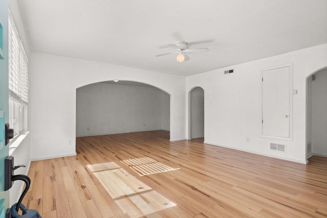 empty room featuring arched walkways, visible vents, light wood finished floors, and ceiling fan