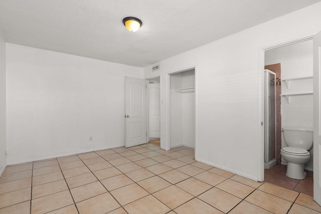 unfurnished bedroom with connected bathroom, a closet, visible vents, and light tile patterned flooring