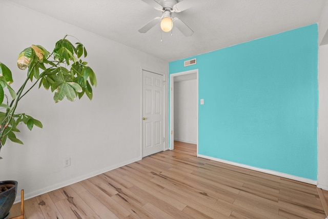 unfurnished room with a ceiling fan, wood finished floors, visible vents, and baseboards