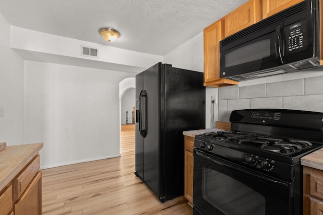 kitchen with tasteful backsplash, visible vents, light wood-type flooring, arched walkways, and black appliances