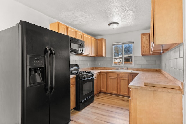 kitchen featuring black appliances, a sink, backsplash, light wood finished floors, and light countertops