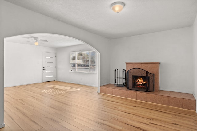 unfurnished living room featuring baseboards, a fireplace, wood finished floors, arched walkways, and a ceiling fan